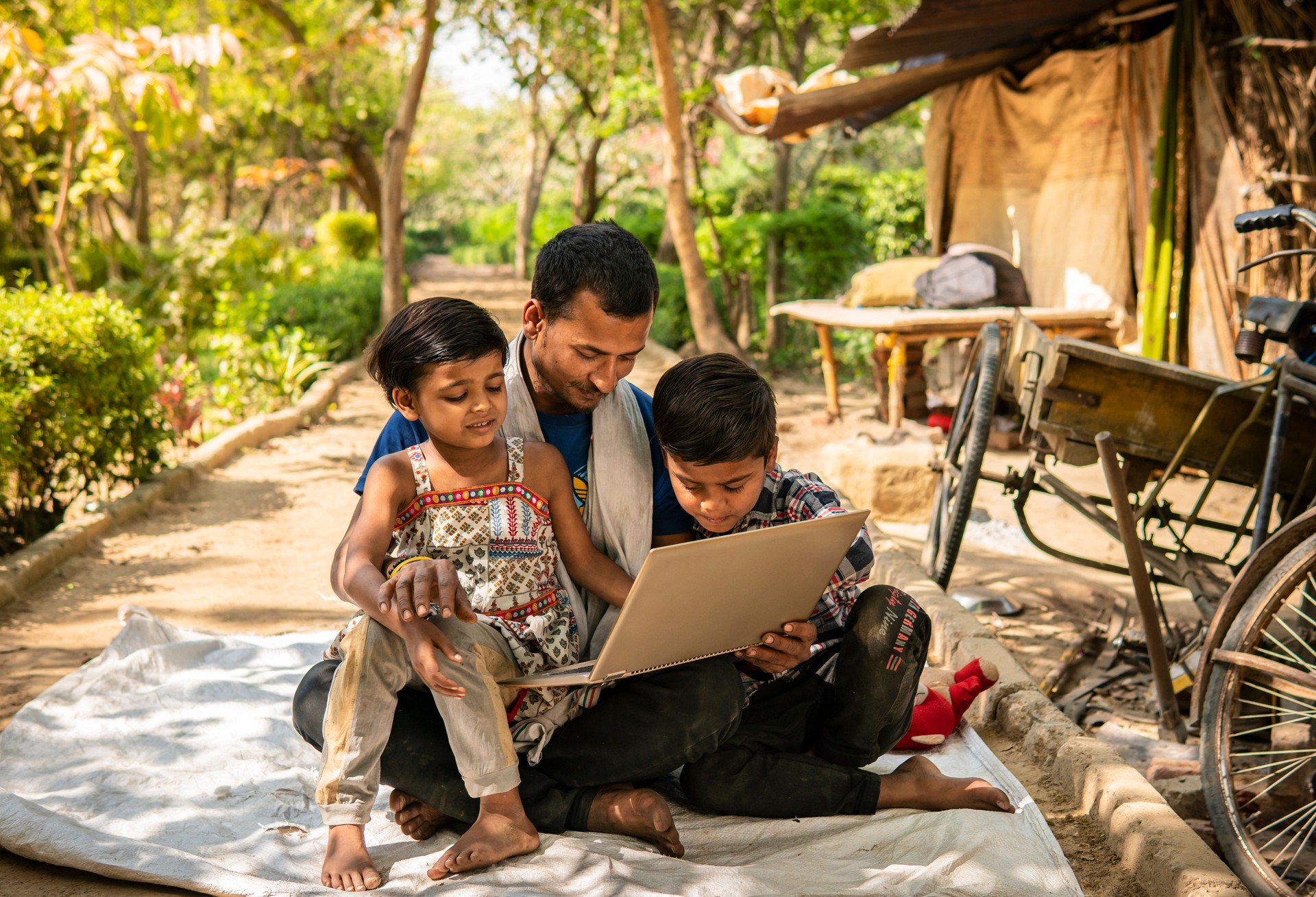 Rural indian father and children sitting together outside their home and using laptop in the village.